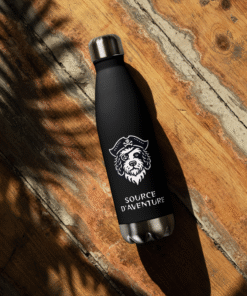 Gourde isotherme enfant Les Chiens Pirates noire avec logo Source d’Aventure posée sur surface en bois